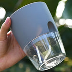 Hand holding a gray self-watering planter, showing the clear lower reservoir