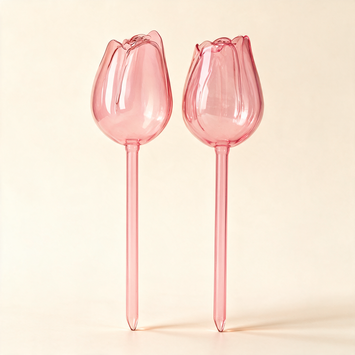 Pair of pink glass tulip-shaped self-watering globes for potted plants.
