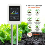 6-in-1 digital soil meter displaying humidity, fertility, temperature, pH and light readings, pushed into soil beside lettuce